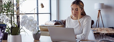 A girl at home, sitting at a table and working on her laptop
