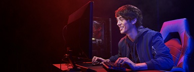A young man playing video games on his computer in a dimly lit room