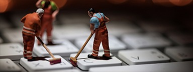 Miniature people cleaning white keyboard computer, with orange lights flickering in the background