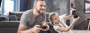 a father and daughter sitting on carpet at home playing video games