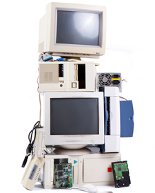 Một chồng màn hình CRT cũ màu be, bộ nguồn PC, vỏ máy tính, máy in và ổ đĩa quang