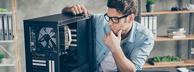 A man sits at a desk with an open PC tower case, pondering its components both in and outside the case.