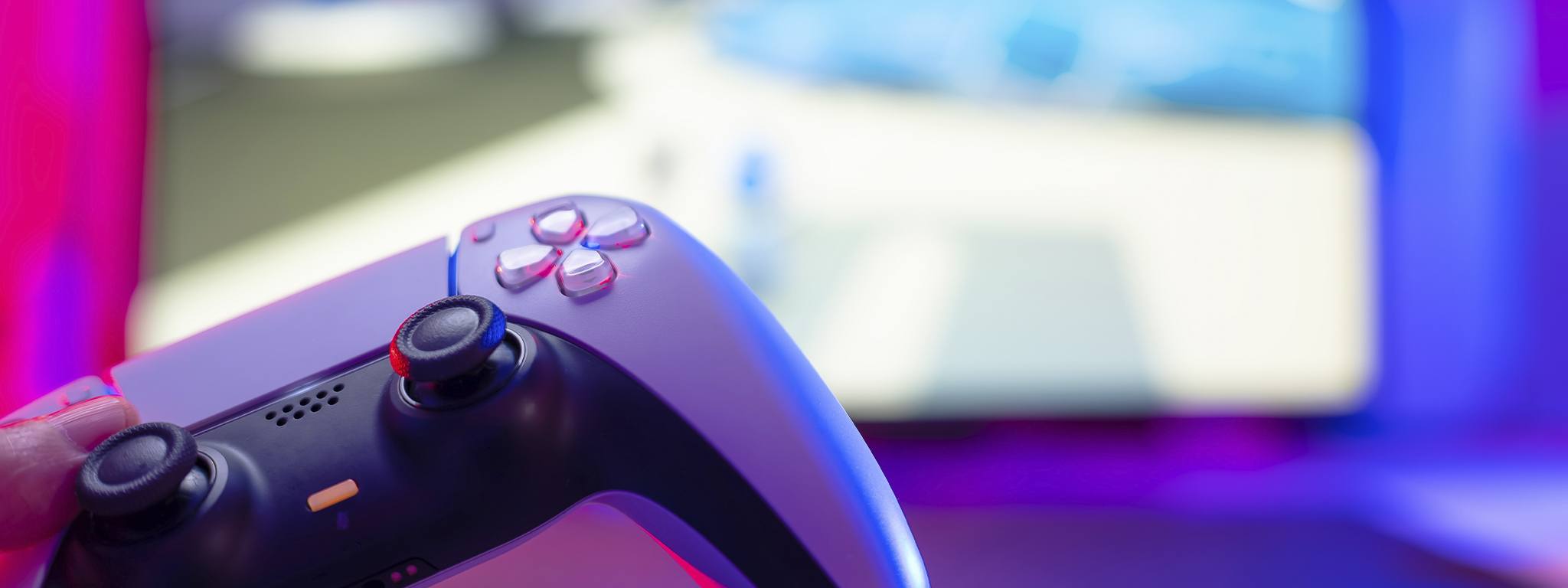 PlayStation 5 控制器的特寫鏡頭，後面有模糊的電視遊戲背景