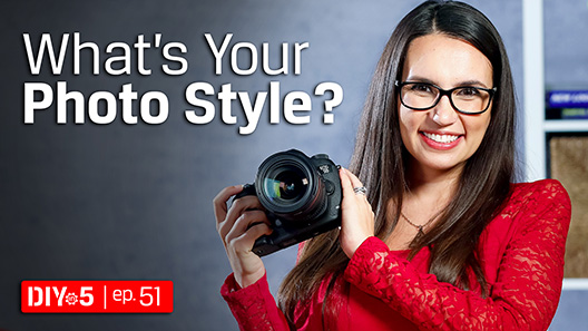 Trisha đang cầm một camera DSLR và mỉm cười.